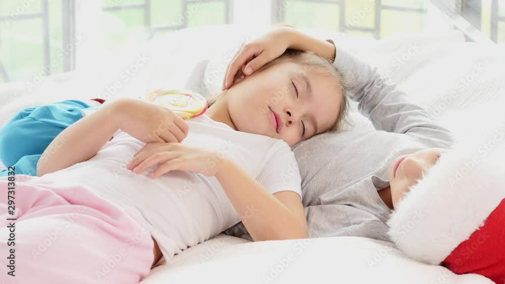 Charming sister is sleeping on the belly of her brother, holding big lollipop on a stick, both looking sweet. Charming sister is sleeping on the belly of her brother, holding big lollipop on a stick, both looking sweet.