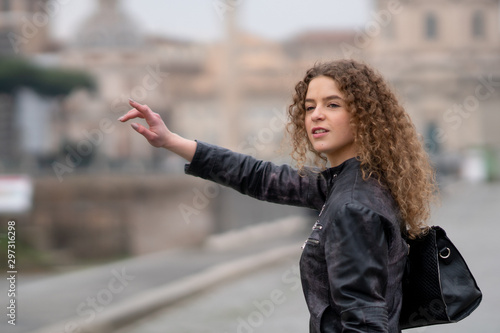 Attractive woman with curly hair and black leather jacket searching for a taxi in Rome, Italy