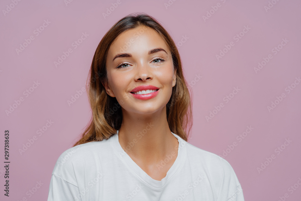 Close up shot of feminine girl smiles gently at camera, wears minimal  makeup, has healthy skin,