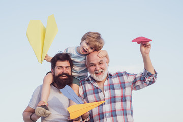 Happy fathers day. Childhood concept. Happy grandfather father and grandson with toy paper airplane over blue sky and clouds background.