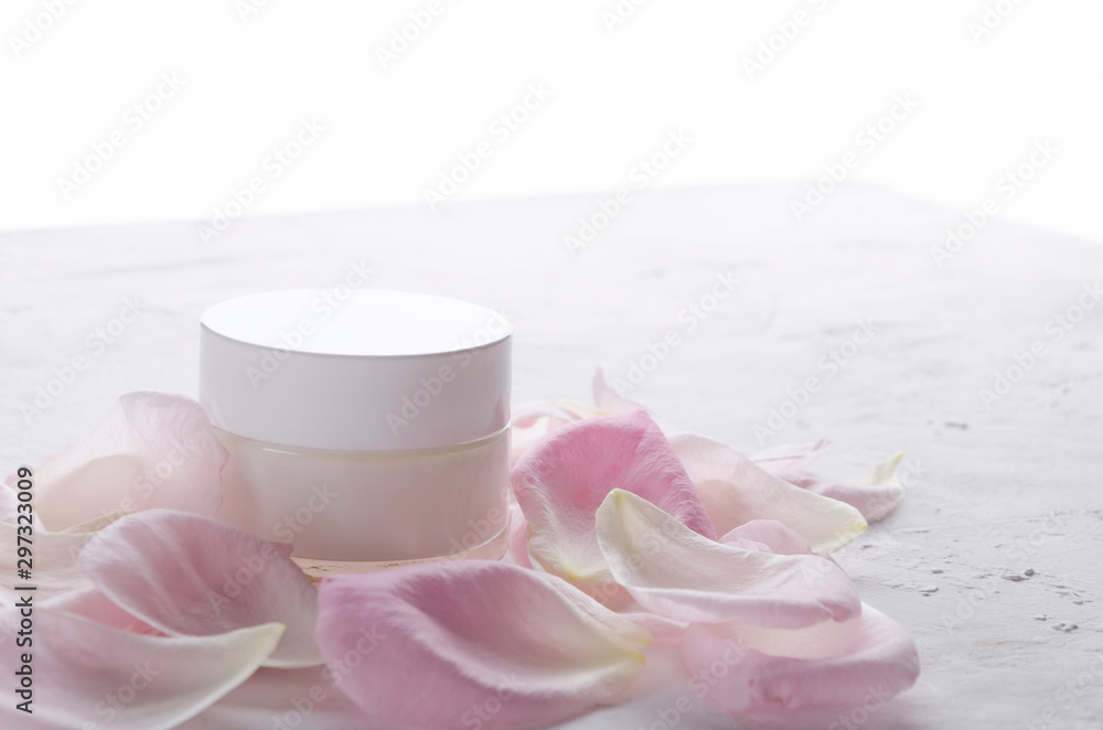 Glass bottle of cosmetics cream, pink petals of roses on the white surface Glass bottle of cosmetics cream, pink petals of roses on the white surface
