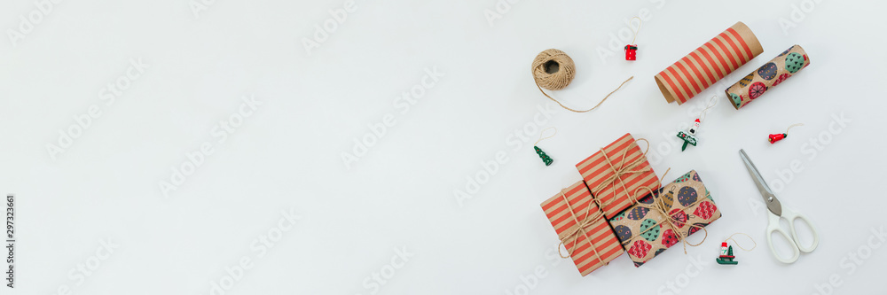 Fototapeta premium Multicolored gift boxes, scissor, Christmas toys, wrapping kraft paper and ball of jute rope. Preparation for holiday. Merry Christmas and Happy New Year concept. White background. Copy spsace.