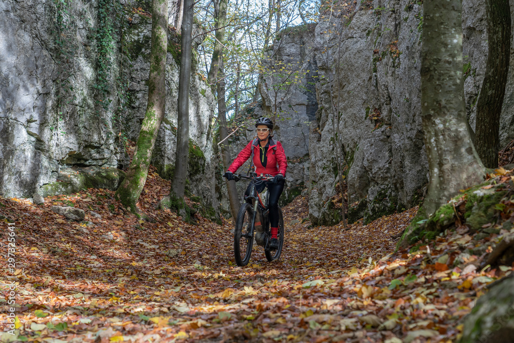 nice senior woman riding her electric mountain bike in the autumnal atmosphere in the Hells Holes of the Swabian Alb near the city of Urach, Baden Wuerttemberg, Germany - obrazy, fototapety, plakaty 