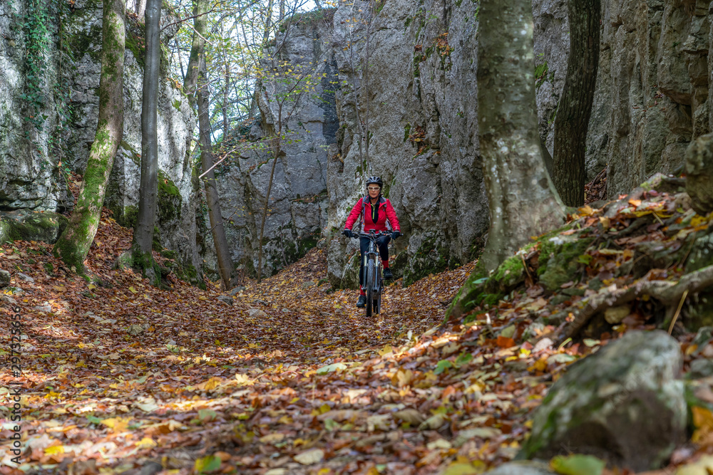 nice senior woman riding her electric mountain bike in the autumnal atmosphere in the Hells Holes of the Swabian Alb near the city of Urach, Baden Wuerttemberg, Germany