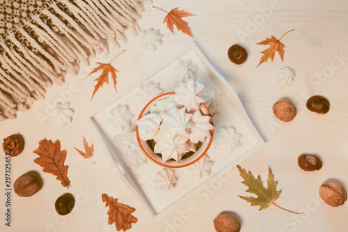 Autumn composition with a cup of meringues, yellow leaves, chestnuts, walnuts and wool blanket on a white wooden background