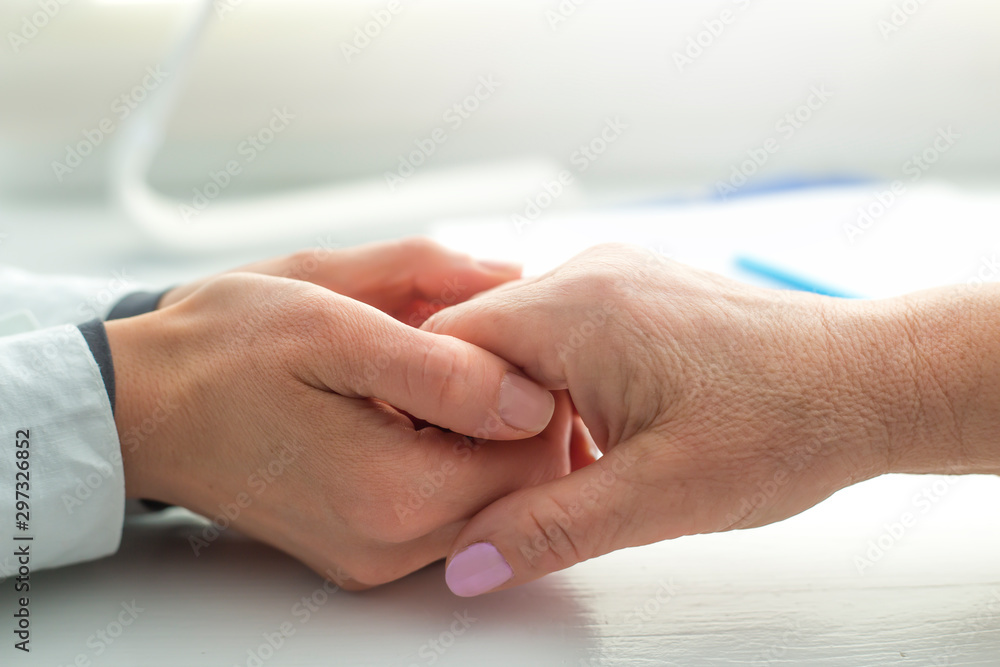 The doctor holds the hand of an elderly woman. A nurse supports an old female patient.