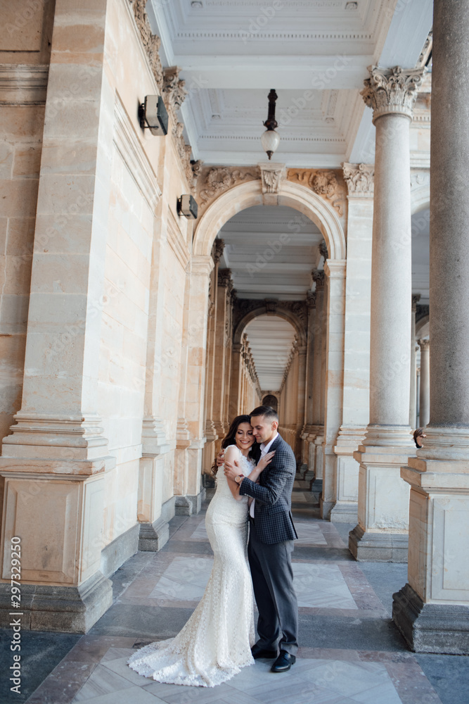 Obraz premium Fashion photo. Young elegant sexy couple hugs, wearing suit and white dress with a train, enjoy their honeymoon, luxury style, love, stylish lovers. Love story. Lifestyle concept.