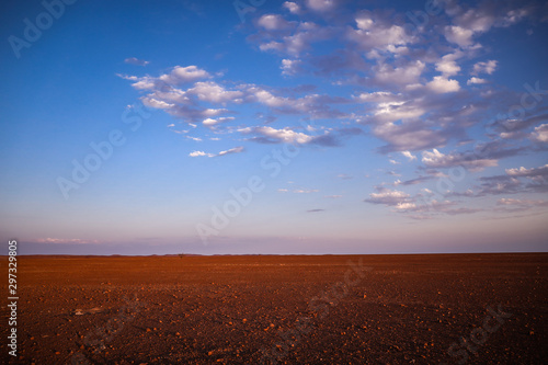 Désert plat et hostile avec une lumière orangée de fin de journée et un ciel bleu et quelques nuages blancs en Namibie - Afrique