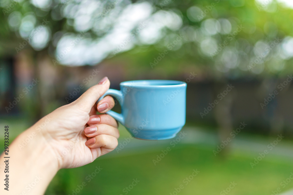 Closeup, girl holds in her hand a blue cup with a drink on a blurred background of a green yard Closeup, girl holds in her hand a blue cup with a drink on a blurred background of a green yard
