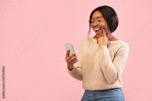 Excited Girl Using Smartphone Holding Finger On Chin, Pink Background