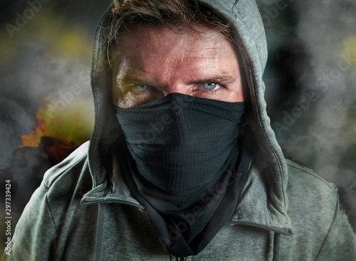 young man as ultra and radical anarchist rioter . furious antifa protester in face mask hostile on street on demonstration in violet riot and chaos between fire and smoke photo