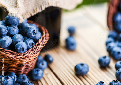 Blueberries on wooden rustic table. Wicker basket full of blueberry in background.