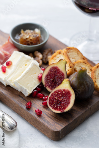 figs with cheese and pomegranate on wooden board and red wine on ceramic background