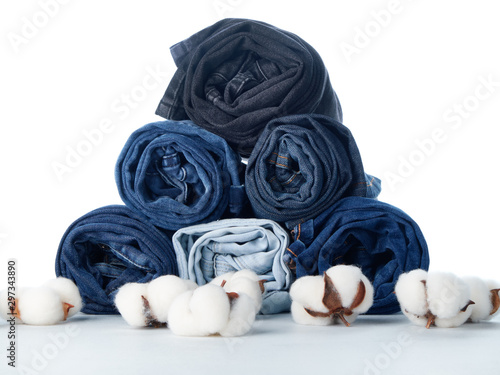 Stack of rolled jeans and cotton flowers on light background