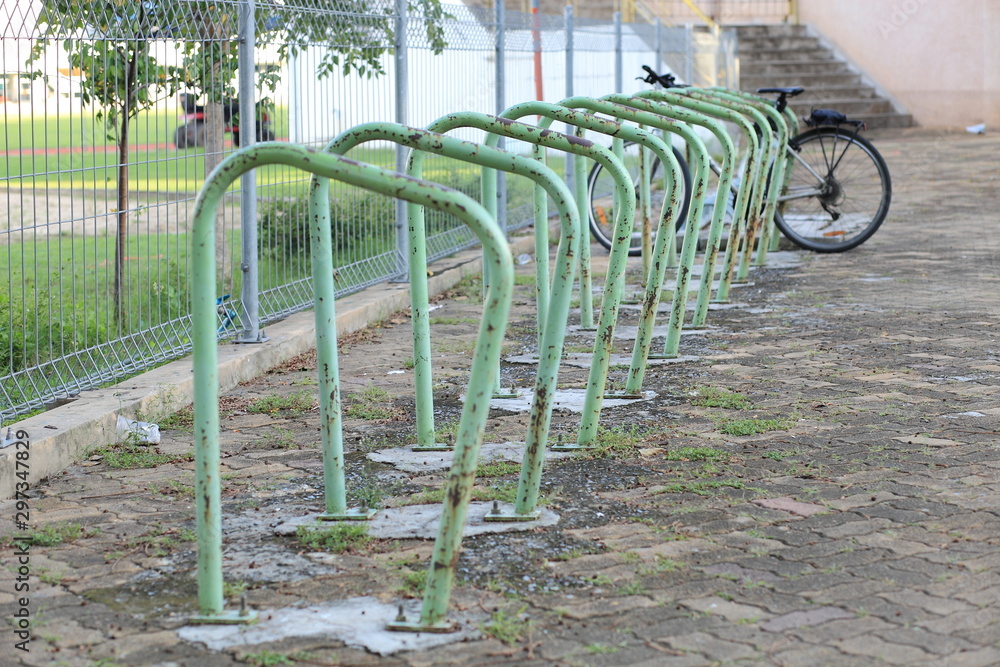 Green steel frame for parking bicycles in public park.