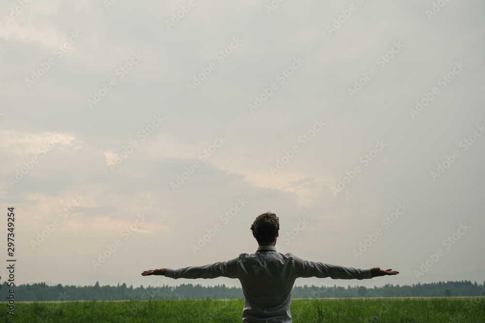 Businessman standing with his arms wide open in the middle of green meadow