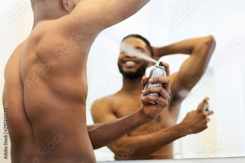 Handsome shirtless african man putting deodorant in bathroom