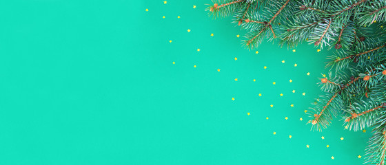 Christmas and Happy new year banner with border of fluffy green fir branches and gold confetti stars sparse on trendy mint background. Simple holiday design template.Top view, flat lay, copy space.