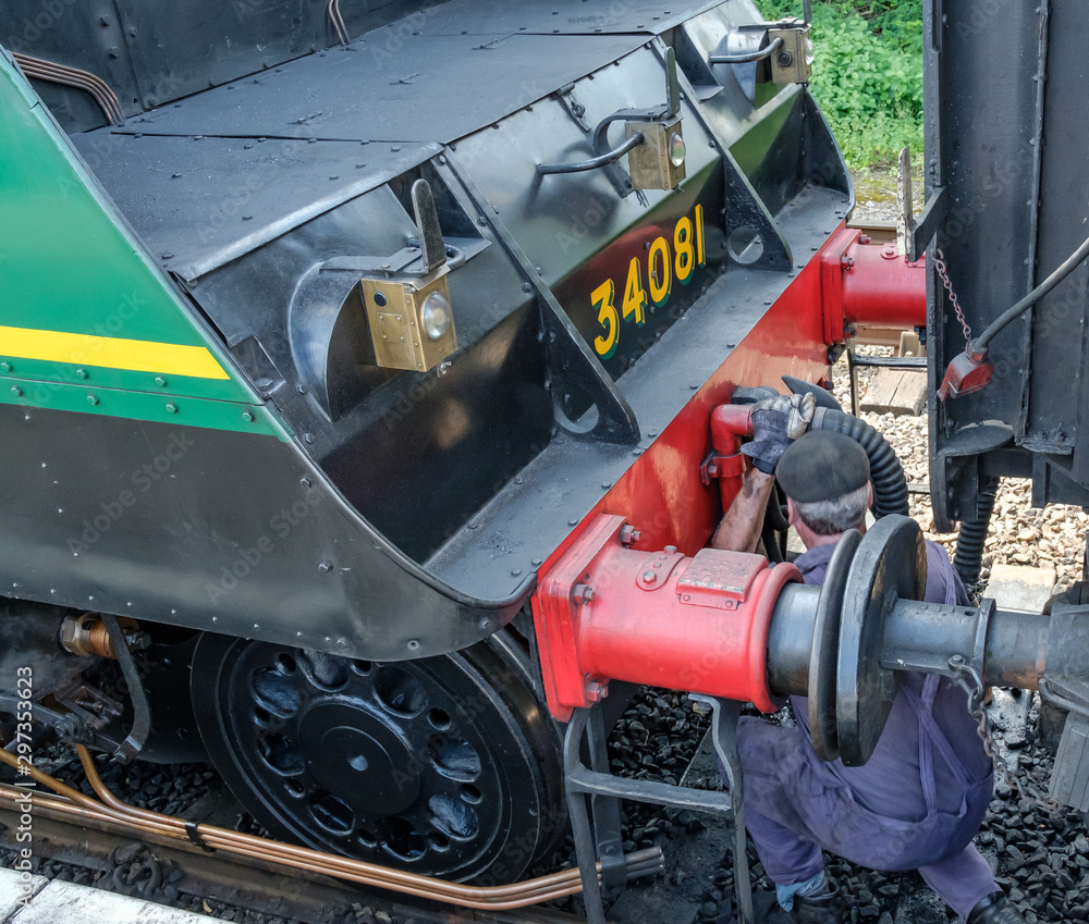 Steam engine driver seen crouching in front of his steam train, de