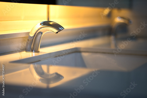 Luxury automatic hand wash faucet / sink with background of orange warming light shade. Housing hardware object photo.  photo
