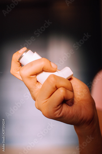 A young woman is using an asthma inhaler device indoor