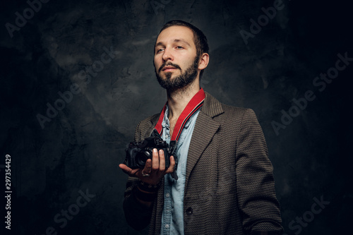 Portrait of bearded young reporter with photo camera at dark photo studio.