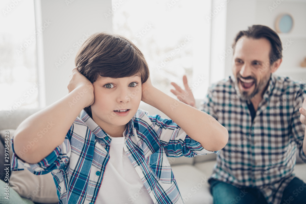 Fototapeta premium Close-up portrait of two guys evil outraged aggressive dad and scared pre-teen son in casual checkered shirt closing ears having fight disagreement in light white modern style interior house