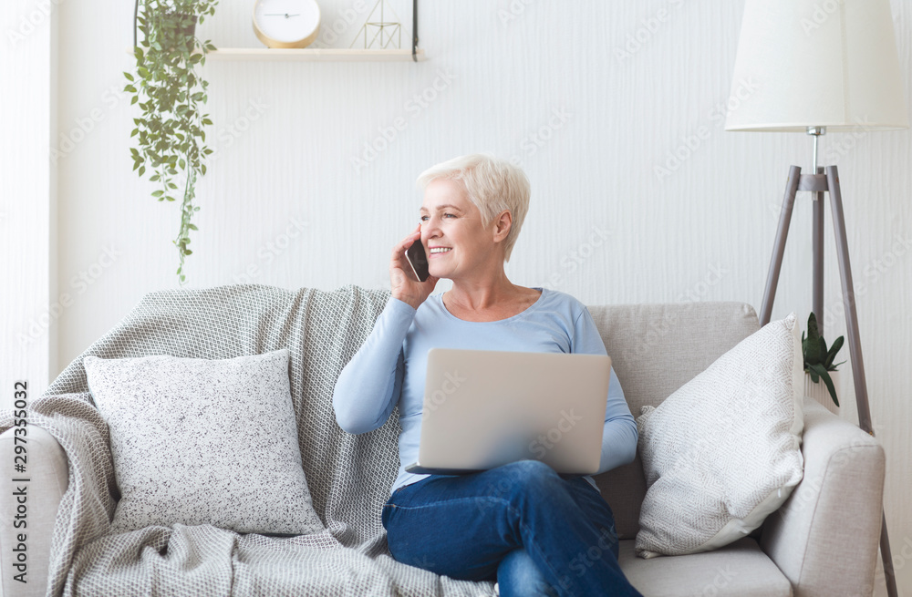 Modern old lady holding laptop and talking by phone Modern old lady holding laptop and talking by phone