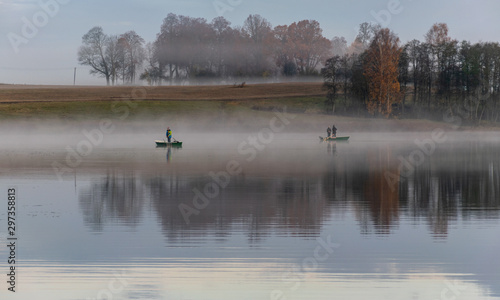 early autumn morning, white mist over water and ground, beautifully colored and blurred tree silhouettes in the background © ANDA