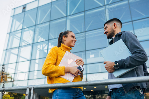 students holding book outdoor in font of university building