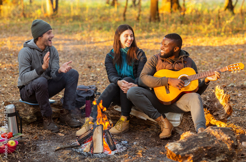 Happy hikers sitting around campfire and singing