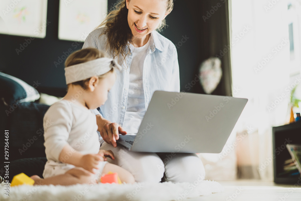 Mother with child sitting on floor watching videos for kids on laptop. Female freelancer working online remotely at home with baby Mother with child sitting on floor watching videos for kids on laptop. Female freelancer working online remotely at home with baby