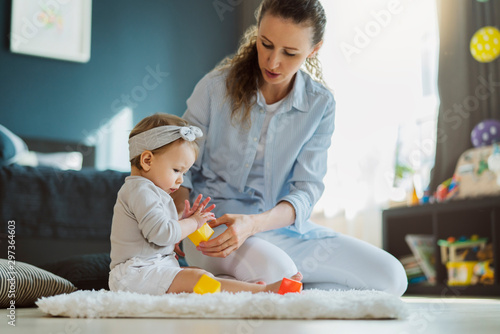 Tablou pe pânză Mother sitting with baby on floor and playing toys