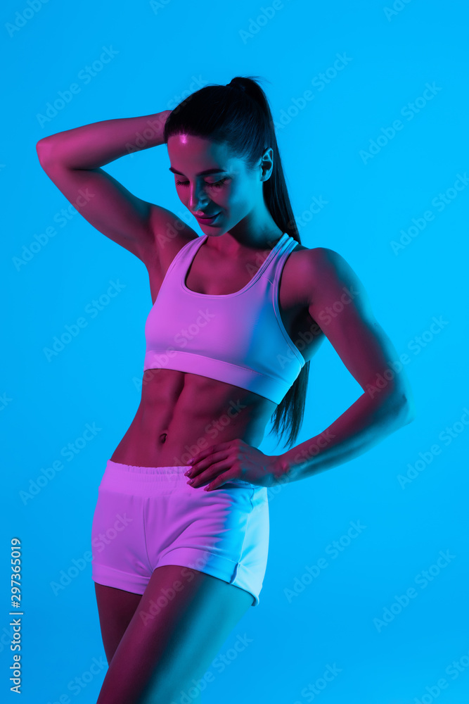 Obraz premium Young sportswoman with perfect body isolated on blue light background
