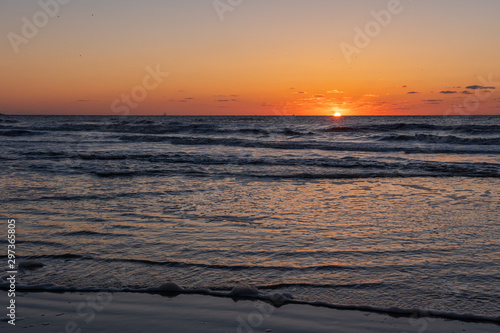 Beautiful orange sunset landscape at the North sea and sky with awesome sun golden reflection on waves as a background. Amazing summer sunset view on the beach.