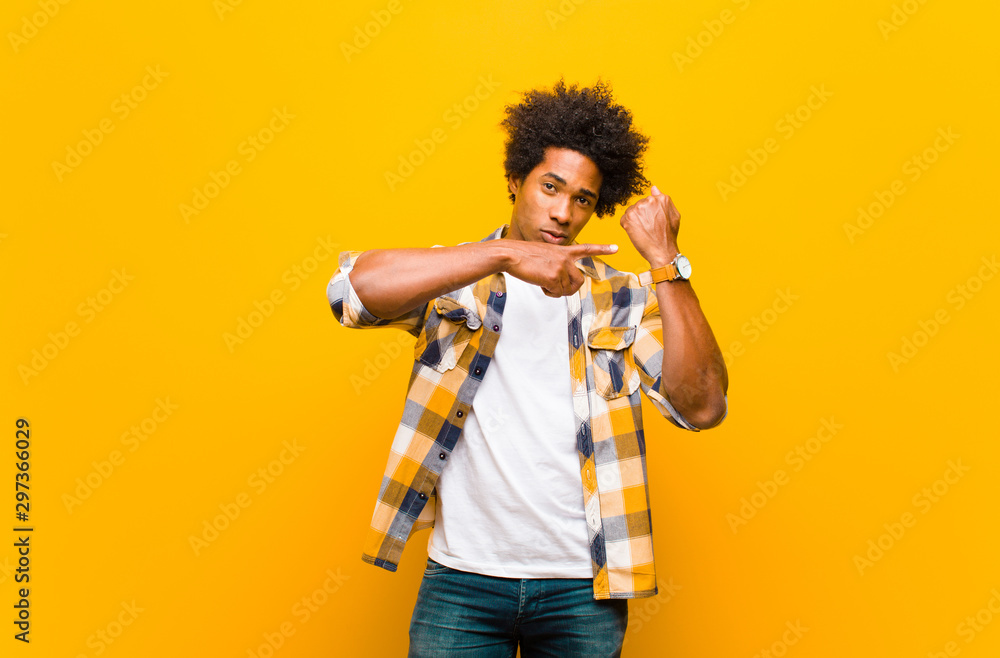 young black man looking impatient and angry, pointing at watch, asking for punctuality, wants to be on time against orange wall - obrazy, fototapety, plakaty 