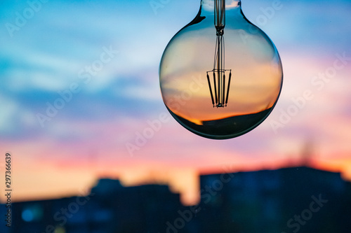 Beautiful defocused sunset in a light bulb. Sunset or sunrise background. Electricity concept. Earth hour. Energy consumption and environmental conservation, energy saving, city in the background 