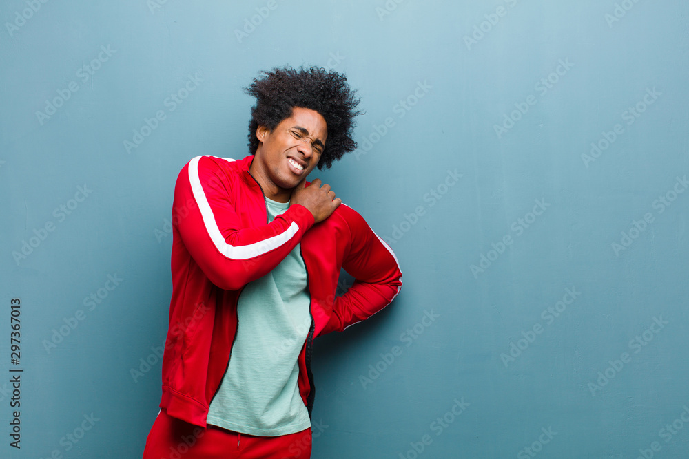 young black sports man feeling tired, stressed, anxious, frustrated and depressed, suffering with back or neck pain against grunge wall - obrazy, fototapety, plakaty 