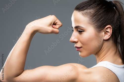 Portrait of a beautiful fitness woman showing her biceps isolated on gray backgr Poster Mural XXL