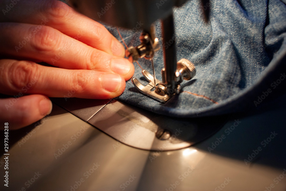Female hands on an old sewing machine sew denim. Close-up Female hands on an old sewing machine sew denim. Close-up