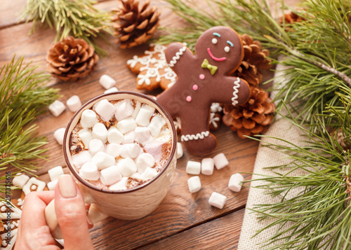 Gingerbread man and hot chocolate with marshmallows, on the background of Christmas tree branches on a wooden table