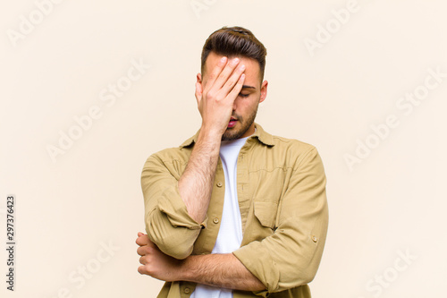 young hispanic man looking stressed, ashamed or upset, with a headache, covering face with hand against isolated background photo