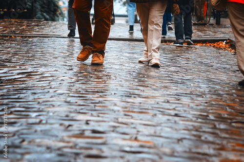 Front view at people feet in shoes walking on wet pavement at rainy autumn day. Copy space. Fall lifestyle. Man and woman walk together at rainy weather outdoors.