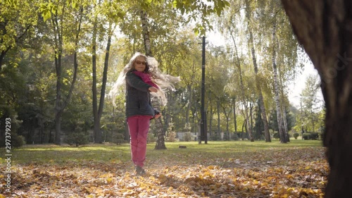 Young cheerful Caucasian girl tossing up yellow leaves in the autumn park or forest and spinning around. Cute teenage schoolgirl in casual clothes spending weekends outdoors. photo