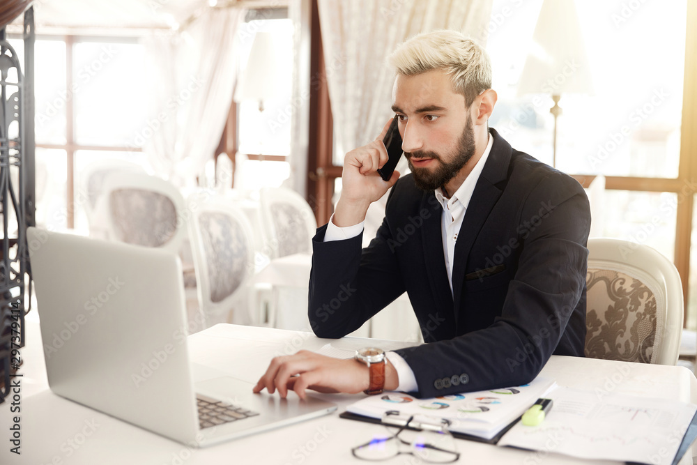 Focused businessman is looking on the screen of a laptop and talking on the cellphone Focused businessman is looking on the screen of a laptop and talking on the cellphone