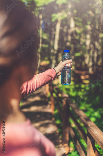 Close up of sportswoman holding bottle of water in forest. Nature and healthy lifestyle concept.