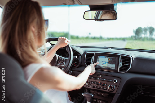 girl in pink car driving car selects an application on touch screen display, turns on selects navigation, chooses route, parks outside city, sets route before starting to move in nature.