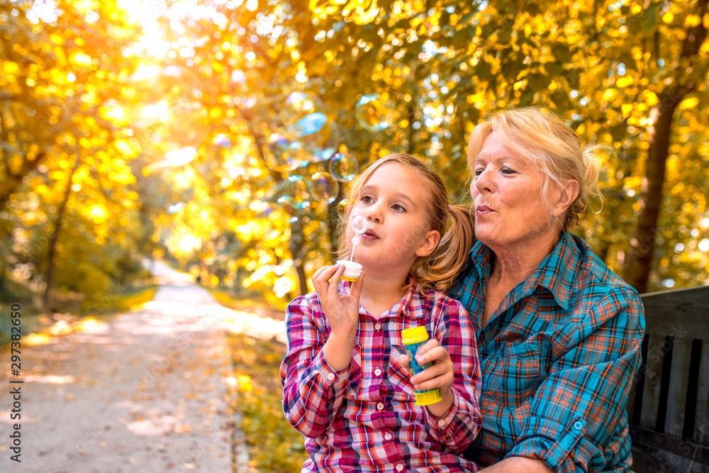 Grandmother and granddaughter enjoying while blowing soap bubbles together in autumn park Grandmother and granddaughter enjoying while blowing soap bubbles together in autumn park