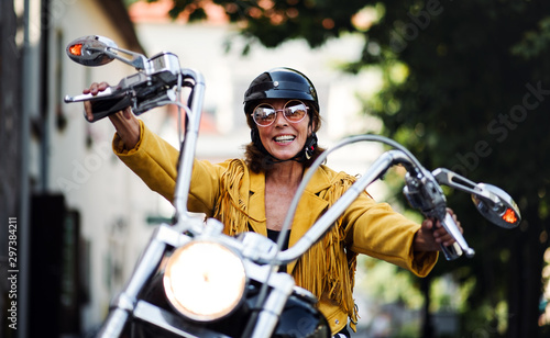 Cheerful senior woman traveller with motorbike in town.