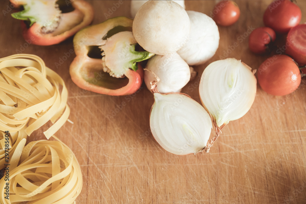 Italian cuisine background, with tomatoes, spaghetti, mushrooms, peppers, onions on a wooden brown board Italian cuisine background, with tomatoes, spaghetti, mushrooms, peppers, onions on a wooden brown board
